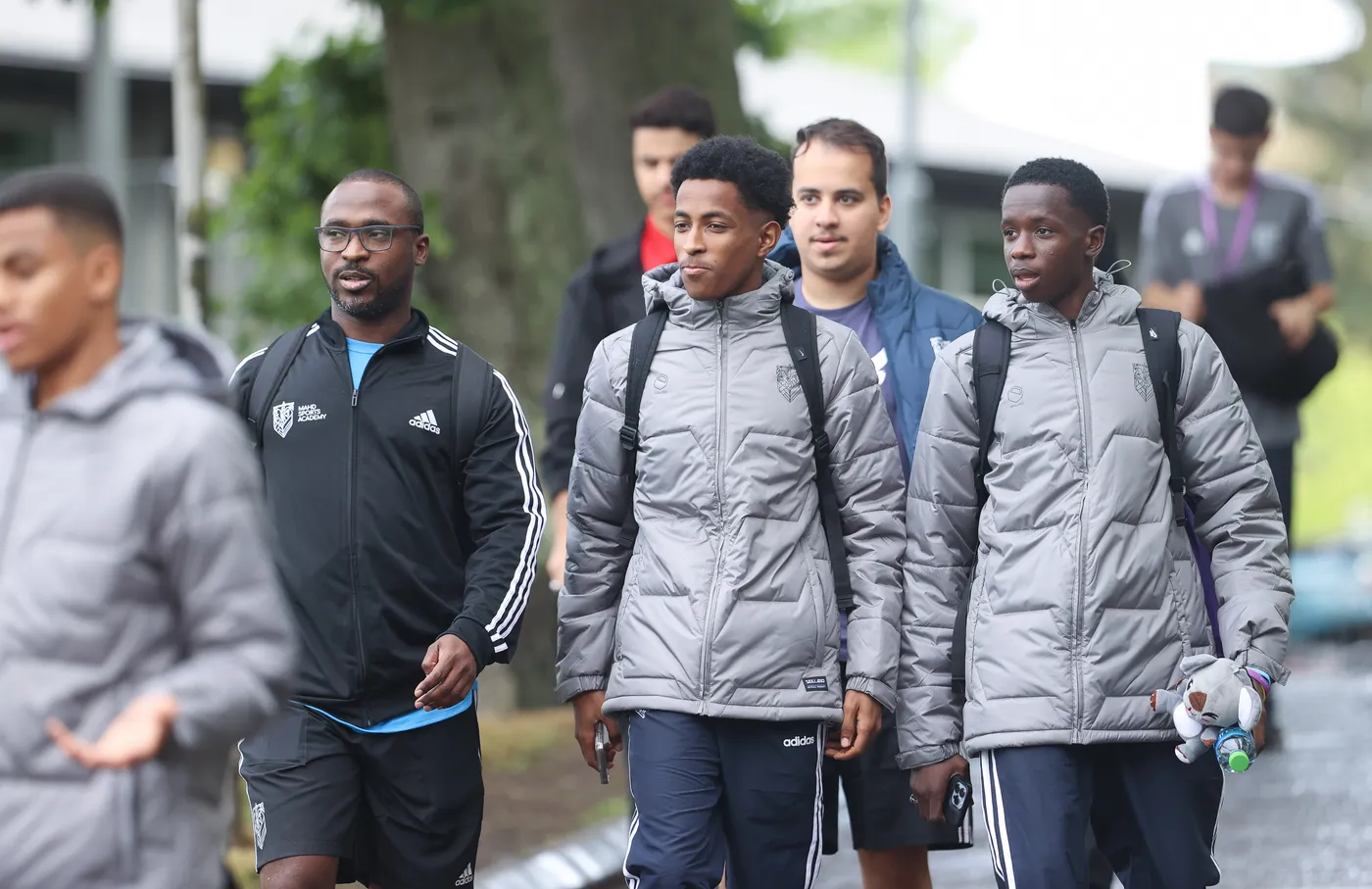 مجموعة من الشباب يسيرون في منطقة خارجية خلال يوم غائم. يرتدي بعضهم سترات دافئة، وبعضهم يحمل حقائب، بينما يبدو أنهم يتحدثون ويمرحون معًا.