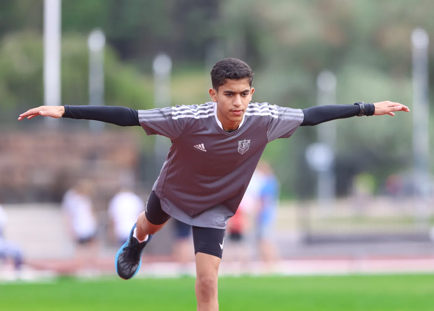 شاب رياضي يتخذ وضعية انطلاق على مضمار رياضي، يرتدي قميصاً رمادياً مع شعار، ويظهر جاداً ومركّزاً. يسعى للمحافظة على توازنه في وضعية دقيقة.