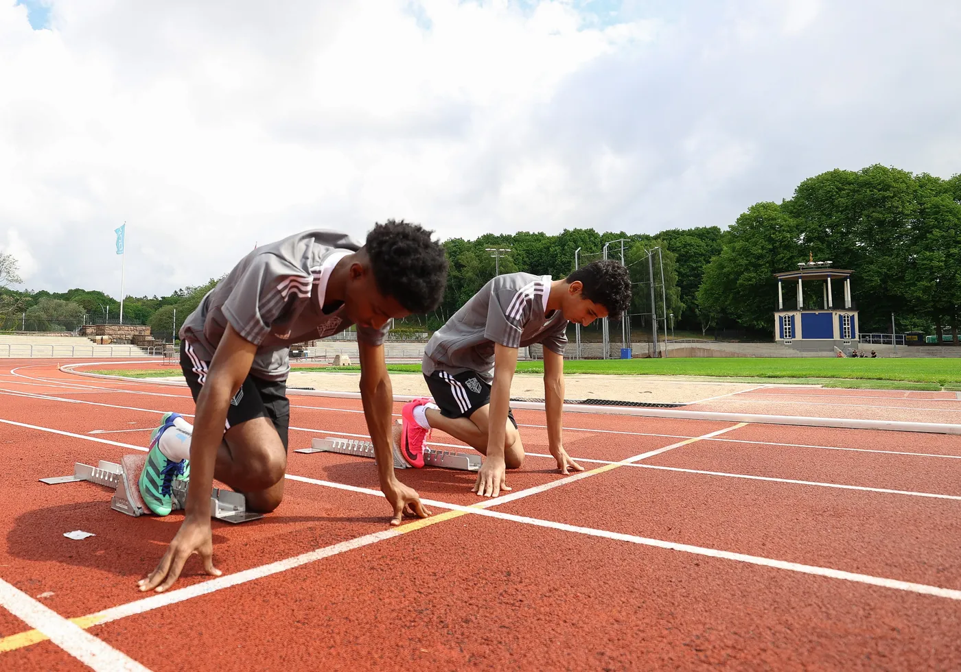 شابان يستعدان للسباق على مضمار رياضي، وهما في وضعية الانطلاق. يتمركز كل منهما على خط البداية مع وضع يديهما على الأرض، في جو من التركيز والجدية.