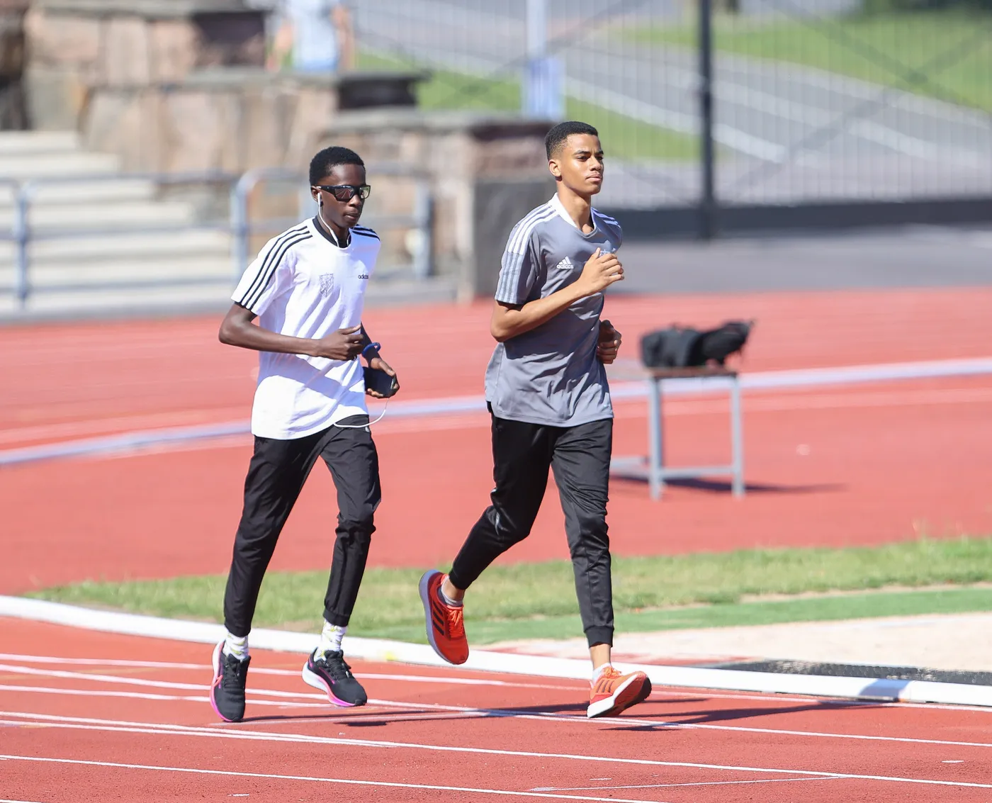 شابان يجريان على مضمار رياضي. الأول يرتدي قميصاً أبيض وسروالاً أسود، بينما الآخر يرتدي قميصاً رمادياً وسروالاً أسود.