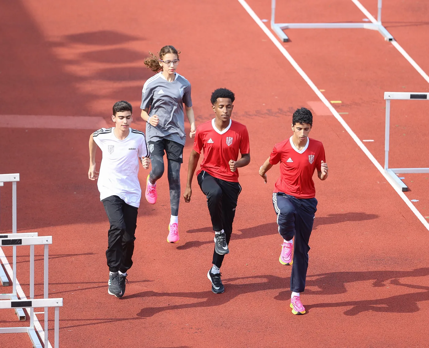 يظهر أربعة شبان يجري إحدهم في مضمار رياضي، حيث يرتدي الثلاثة منهم قمصان حمراء بينما يرتدي واحد قميصًا رماديًا. يبدو أنهم يتدربون على العدو بسرعة عالية.